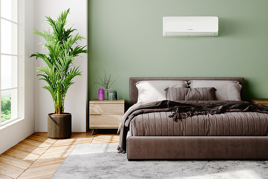 Air conditioning unit on a sage green bedroom wall above a styled bed